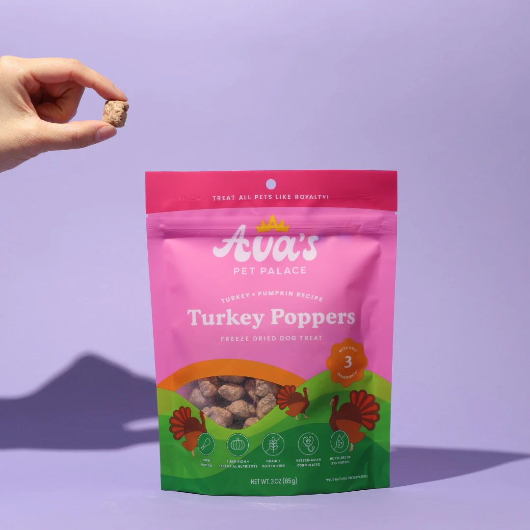 Ava's Pet Palace Turkey Poppers freeze dried turkey dog treats in a pink and green resealable bag with a hand holding one treat