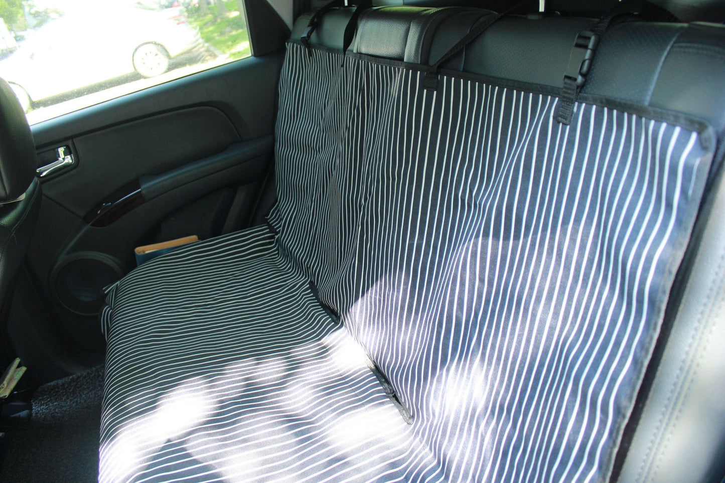 Striped black and white pet car seat protector installed on a car's backseat for pet safety and cleanliness