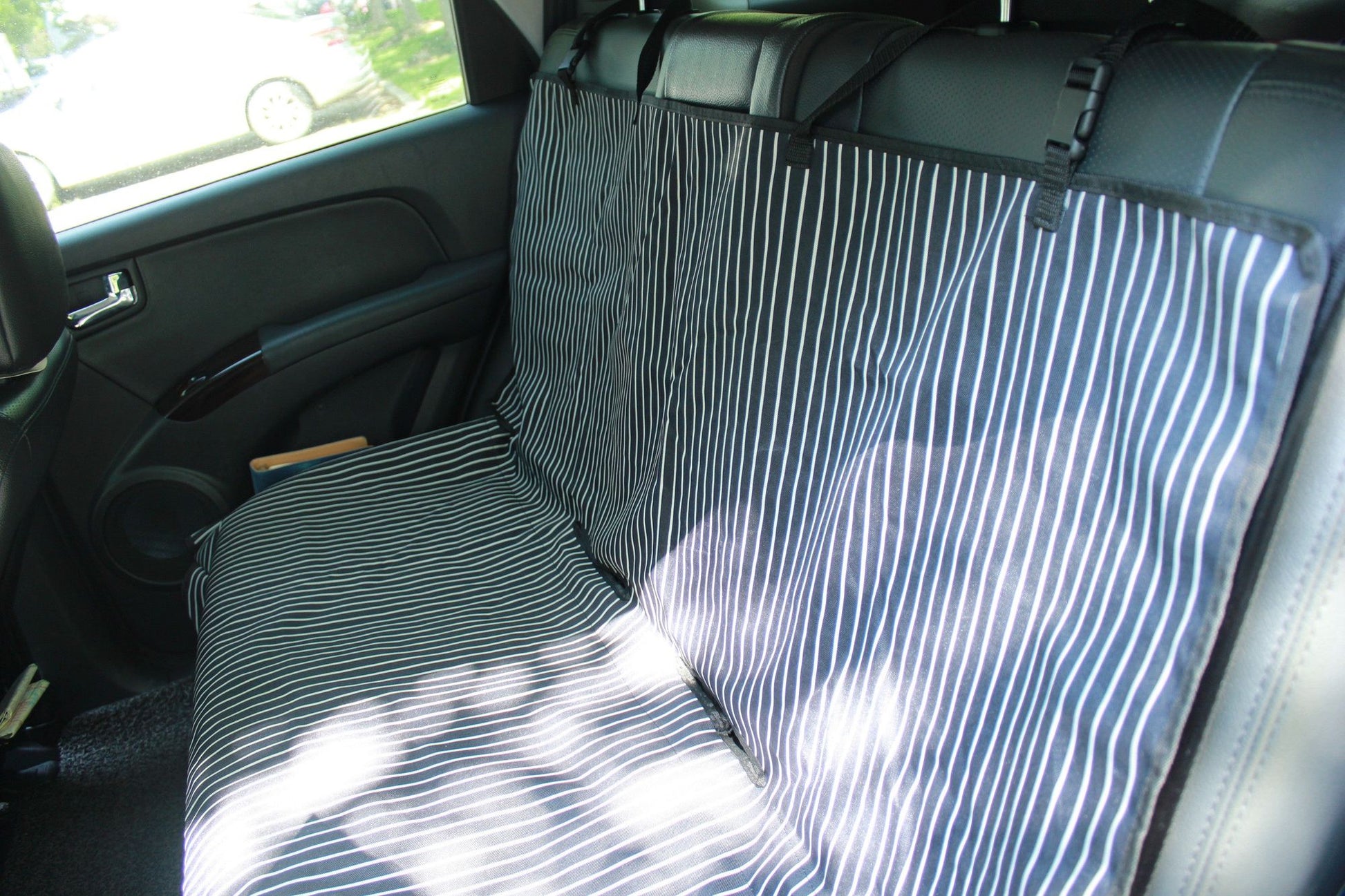 Striped black and white pet car seat protector installed on a car's backseat for pet safety and cleanliness