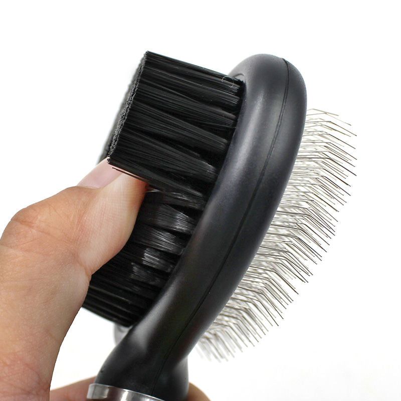 Hand holding black dual-sided pet grooming brush with soft bristles and metal pins
