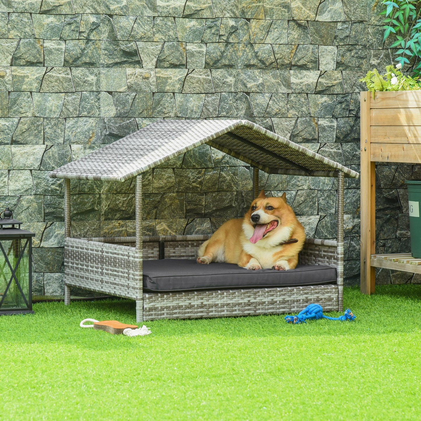Elevated wicker dog house with a roof and cushion featuring a happy dog lying on green lawn
