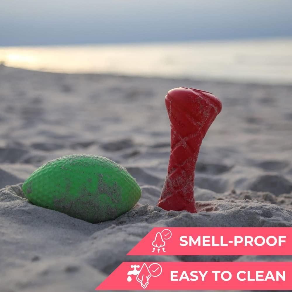 Red and green floating dog fetch toy partially buried in sand on the beach with smell-proof and easy to clean features