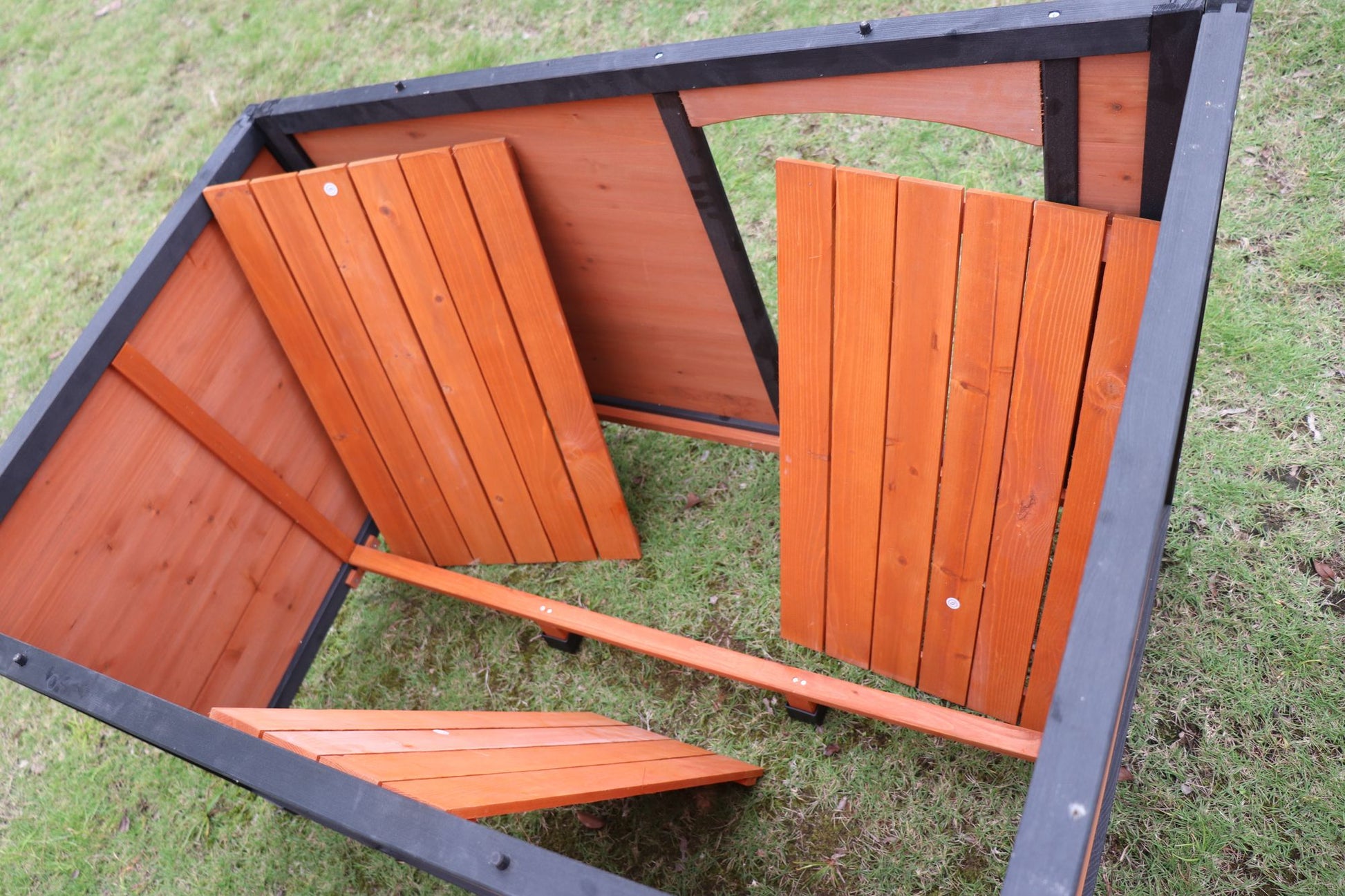 Large weatherproof dog house made of sturdy wood with black frame on grass
