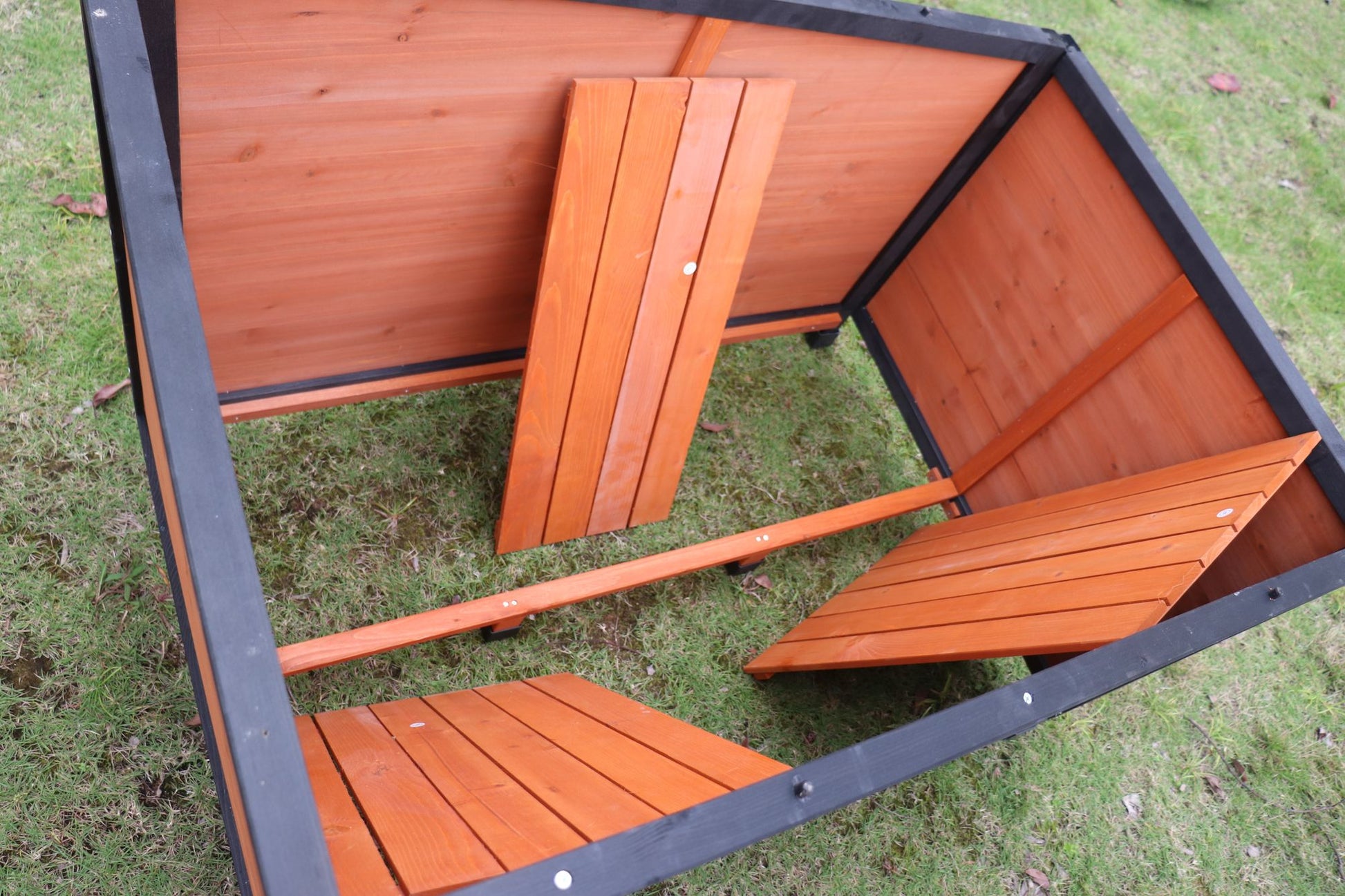 Large weatherproof dog house frame with wooden panels and black metal edges on grass