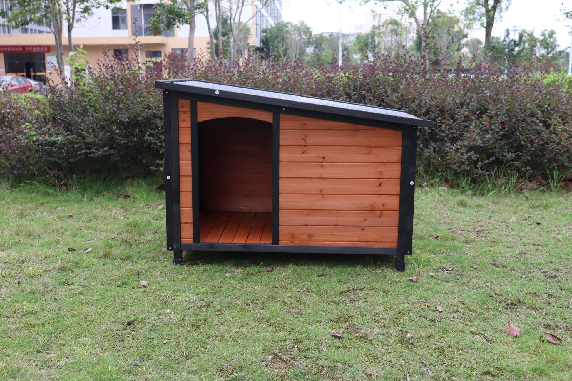Large weatherproof dog house with wooden panels and black frame on green grass