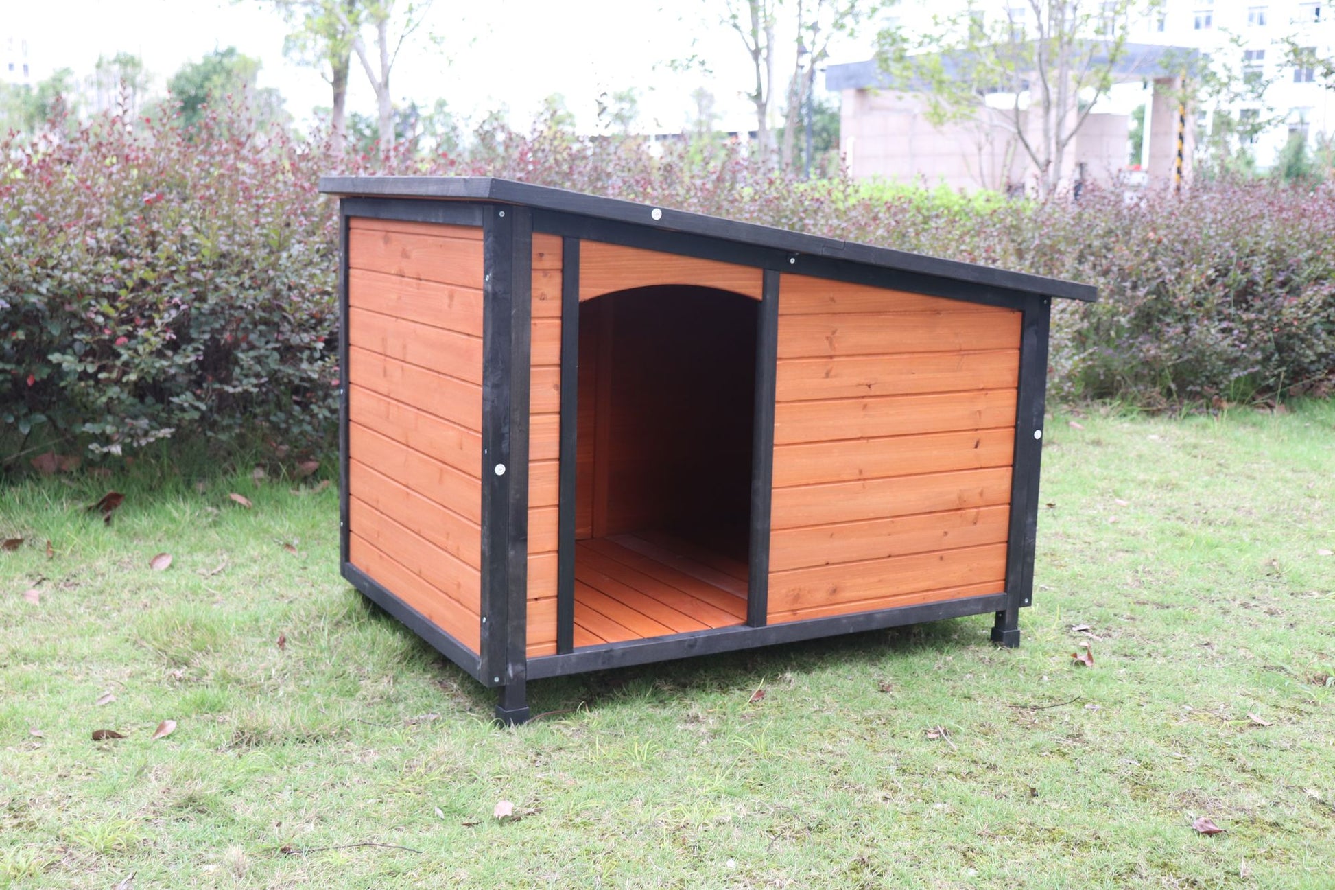 Large weatherproof dog house made of wood with black trim standing on green grass outdoors