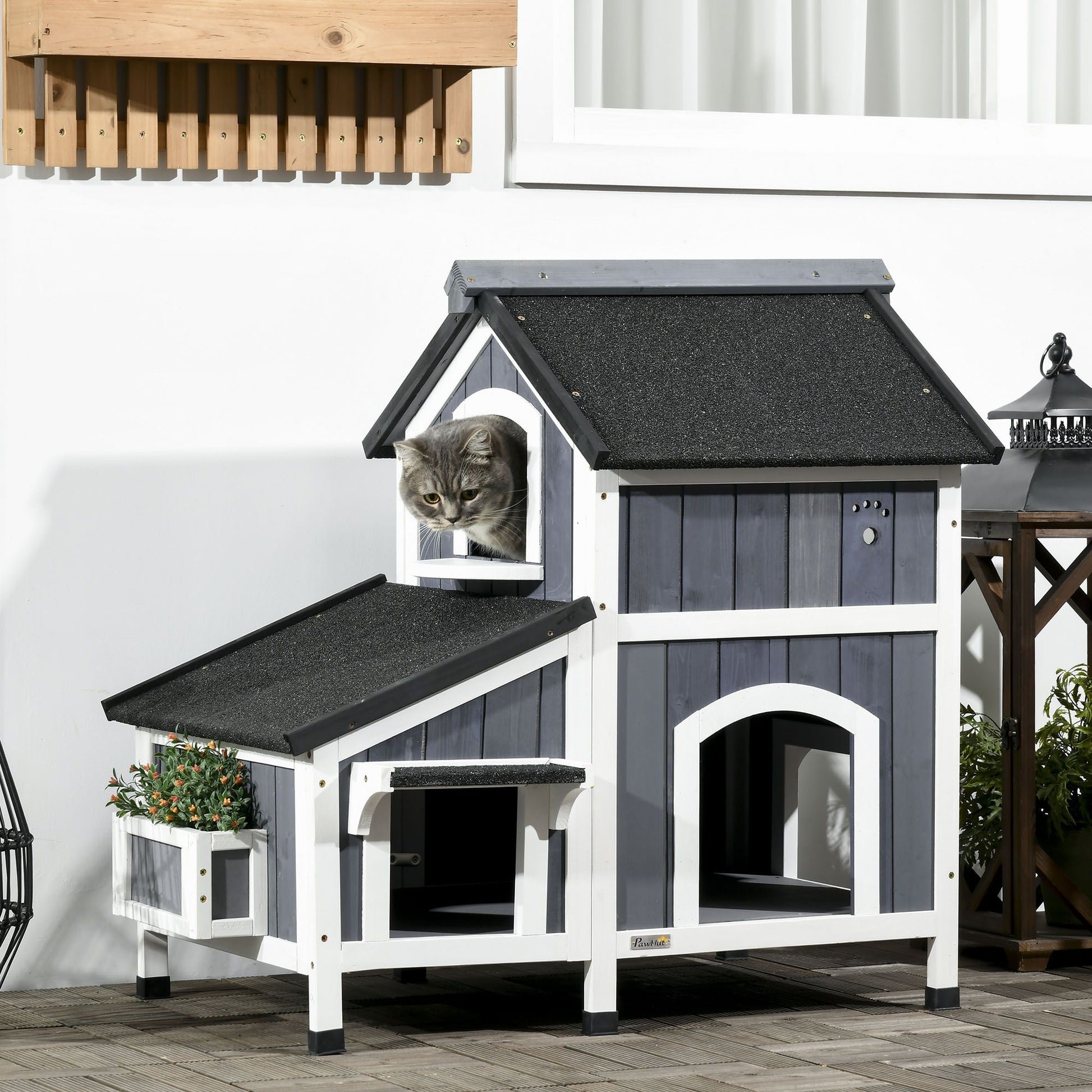Outdoor cat house with flower pot in gray and white wood with a cat sitting inside the upper window