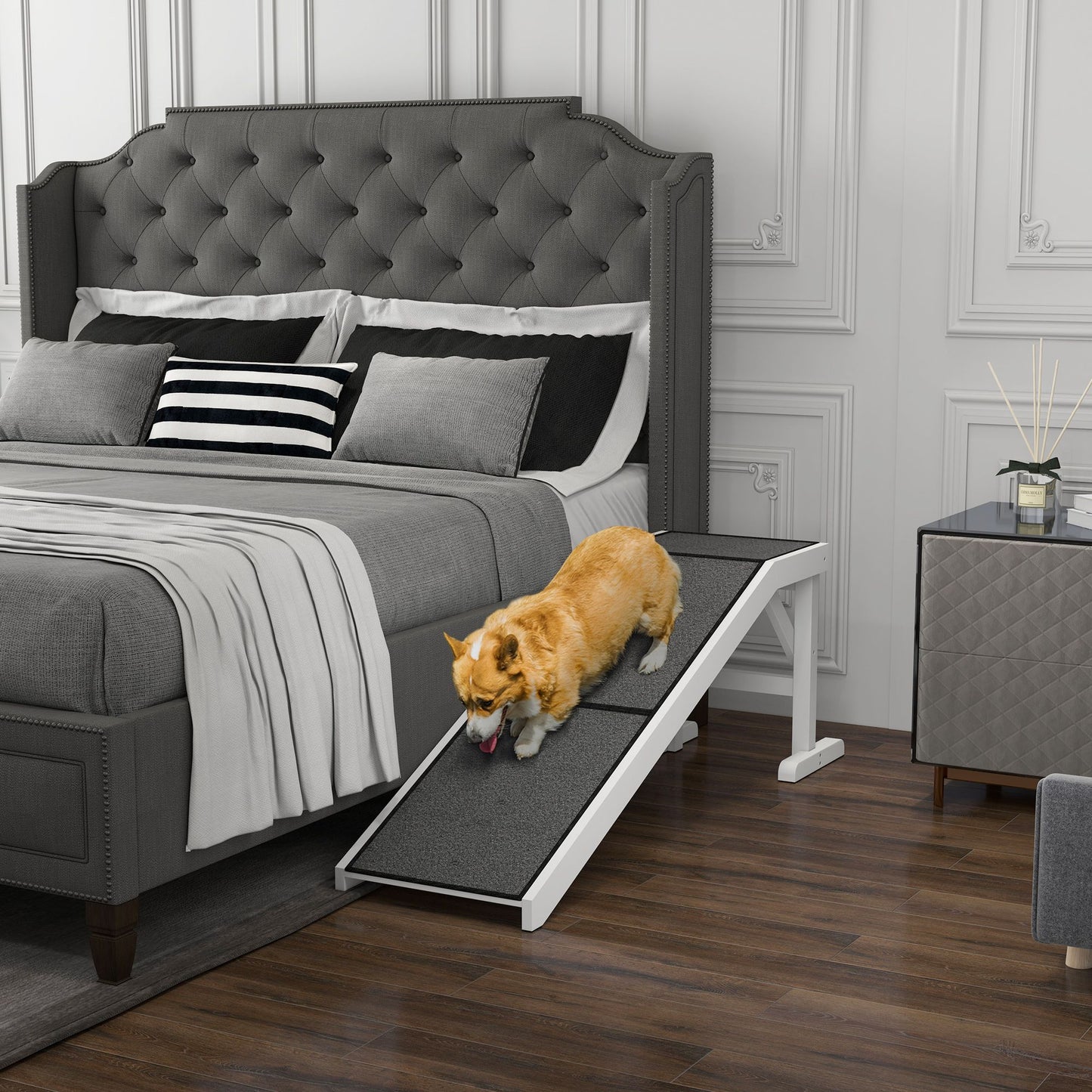 Small dog using a pet ramp for dogs and cats to climb onto a gray upholstered bed in a modern bedroom