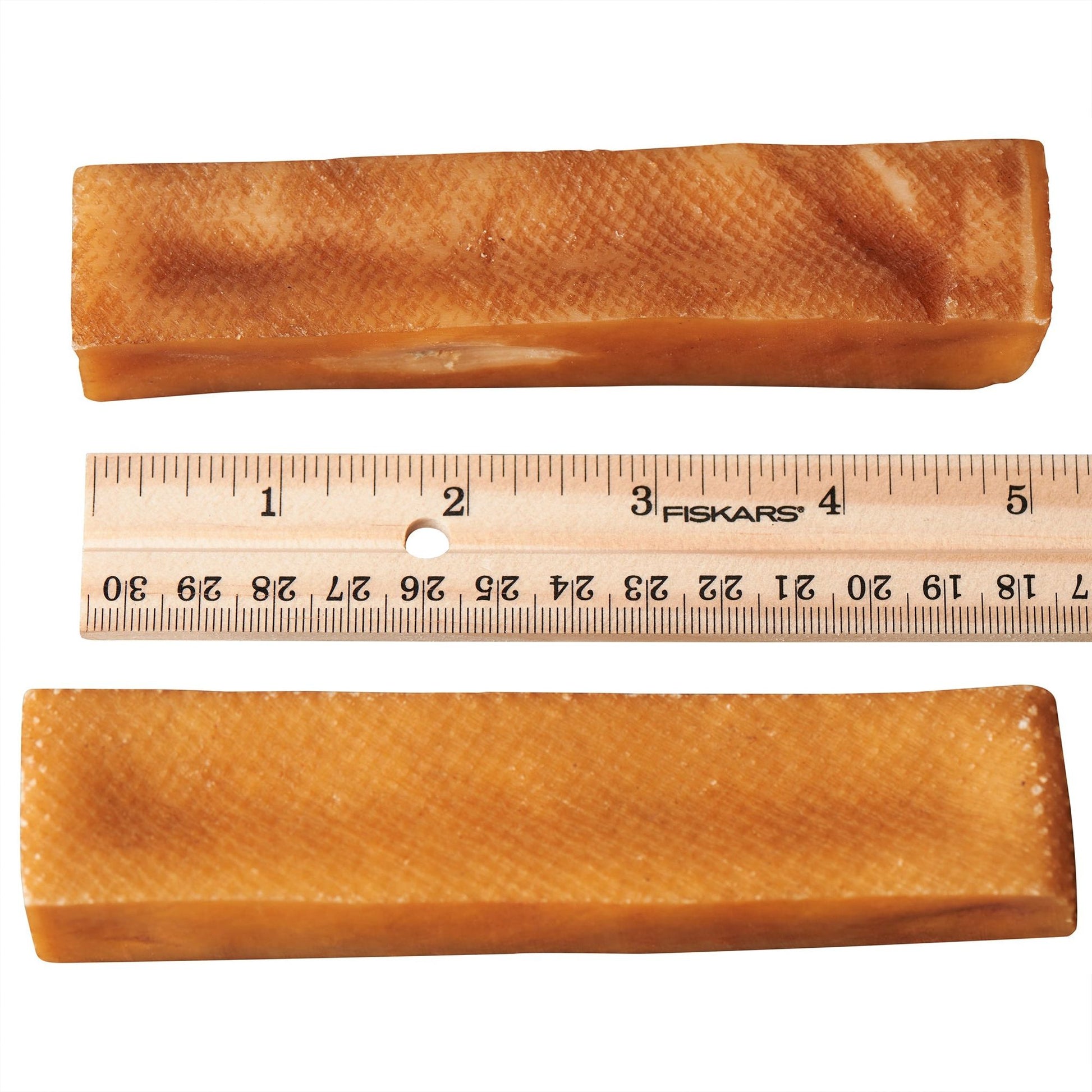 Two rectangular himalayan yak cheese dog chew treats placed above and below a wooden ruler showing size