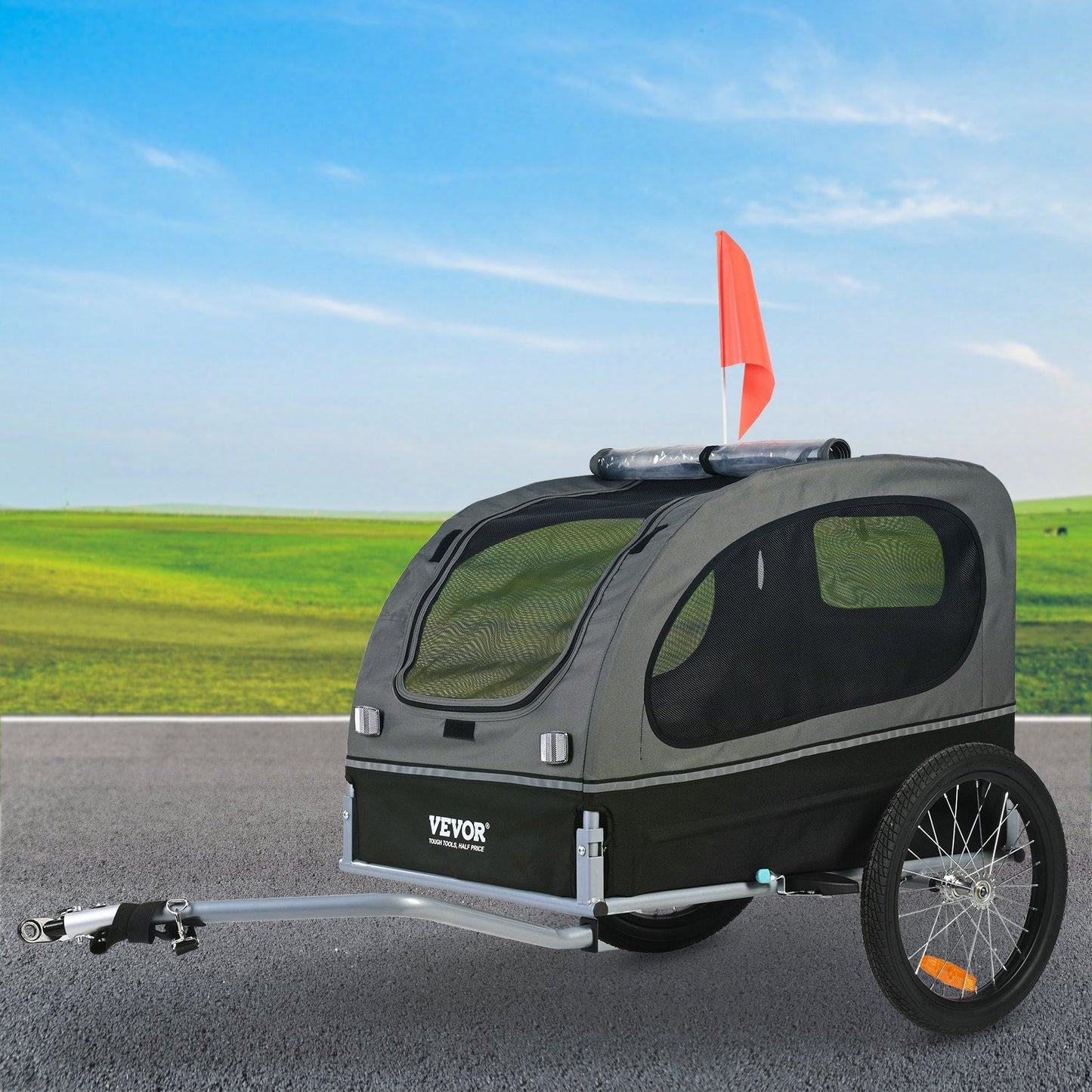 Gray dog bike trailer for large dogs with mesh windows and safety flag attached on a paved road