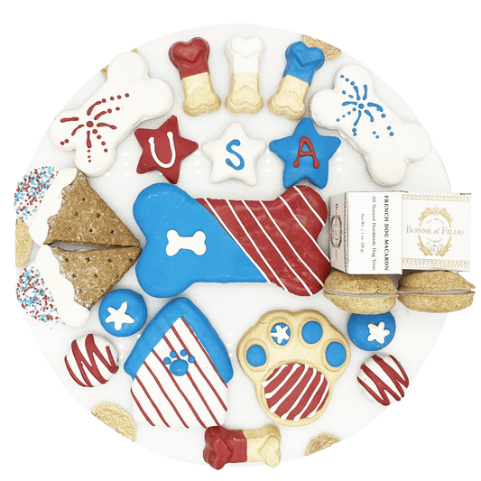 USA themed dog treats in red white and blue colors shaped like bones stars and paws on a white plate