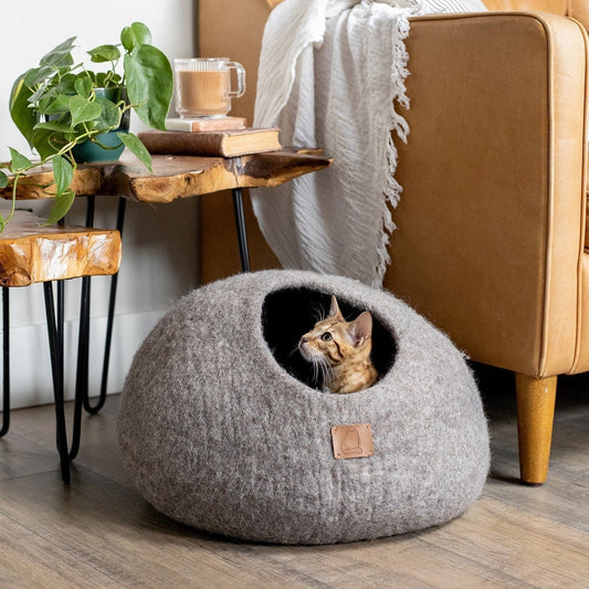 Earth brown pet cave with a cat inside placed next to a leather couch and wooden side tables
