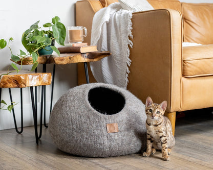Cozy earth brown pet cave next to a tan sofa with a small spotted cat sitting beside it
