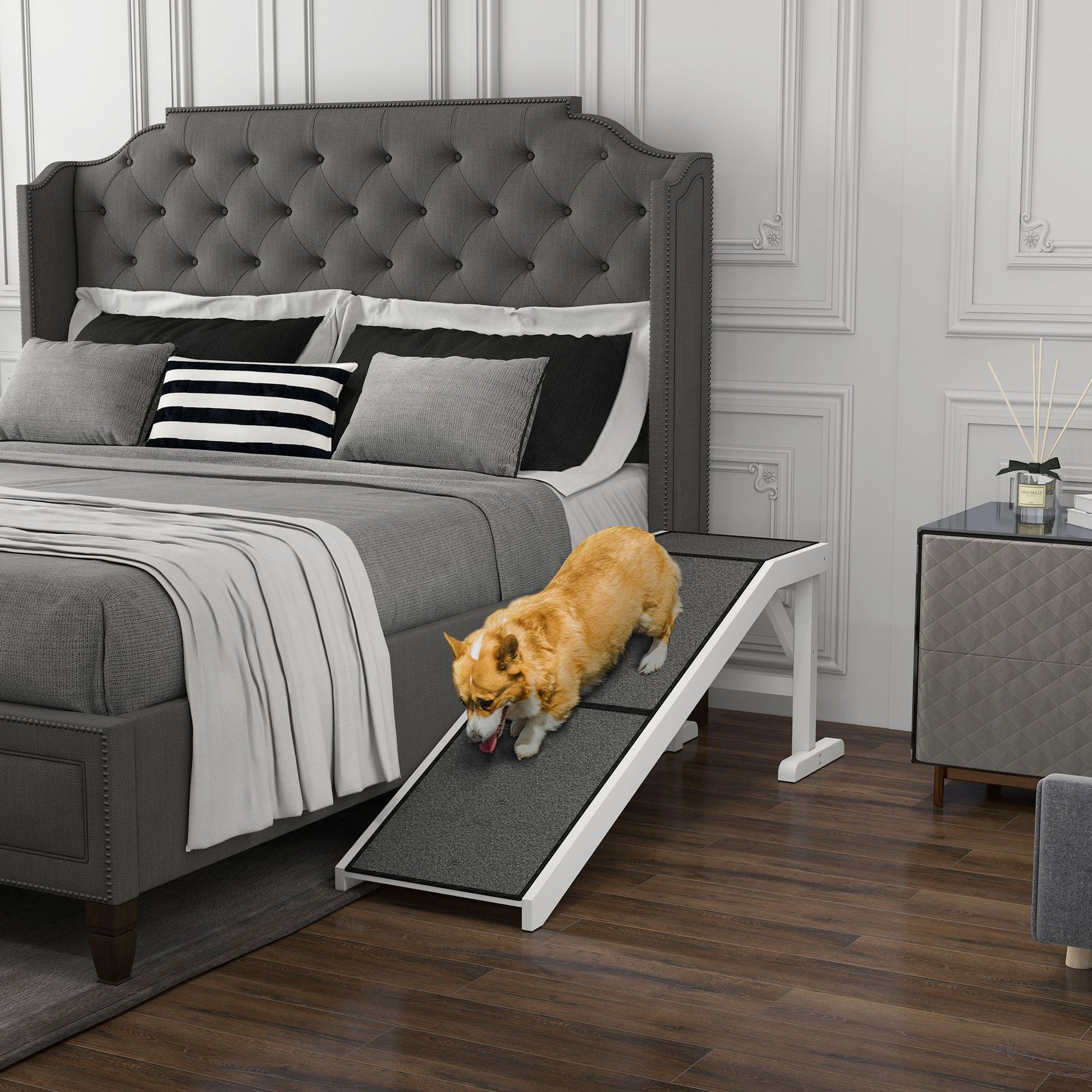 Small dog using a pet ramp for dogs and cats to climb onto a gray upholstered bed in a modern bedroom