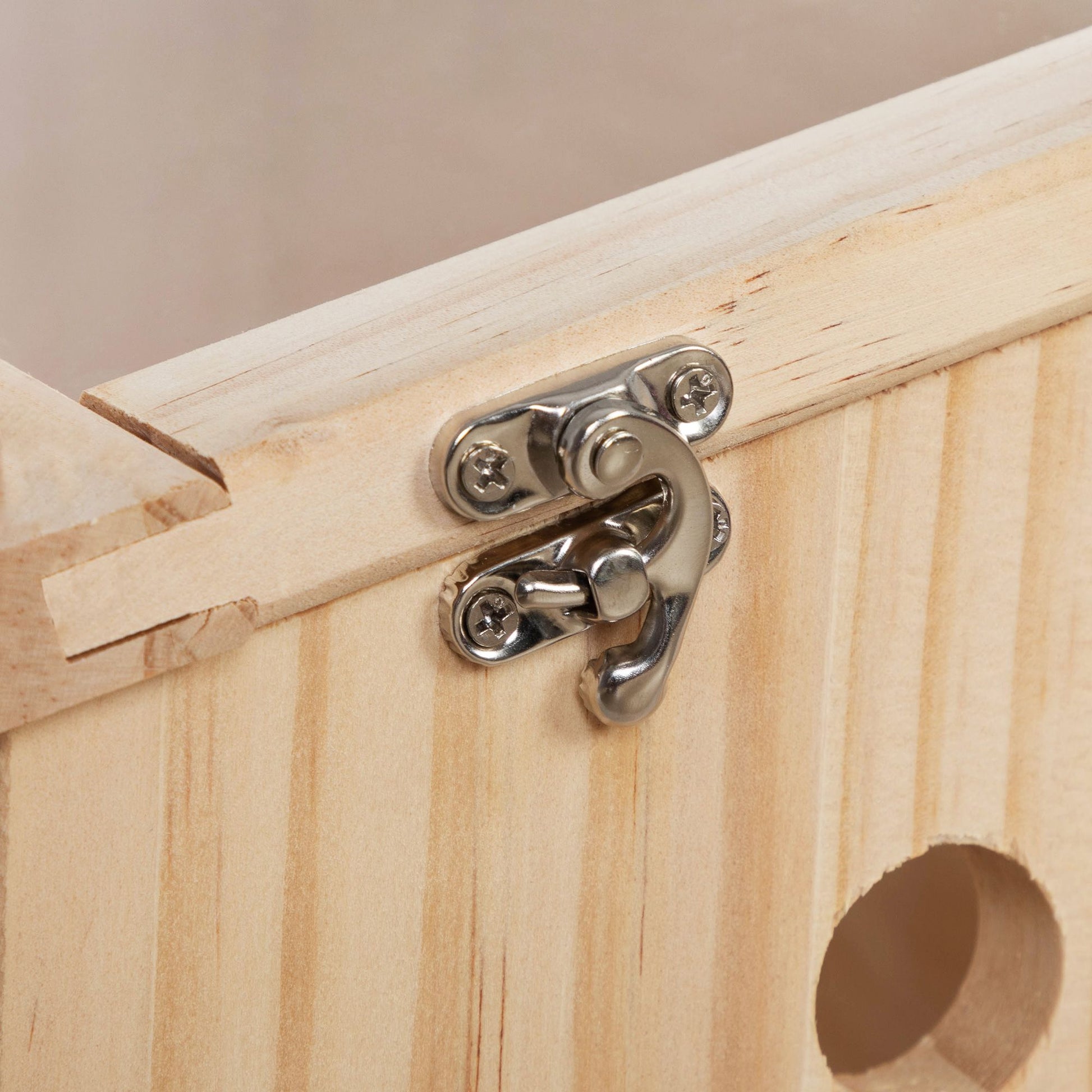 Close-up of metal latch on a transparent wooden hamster cage showing natural wood texture and circular hole